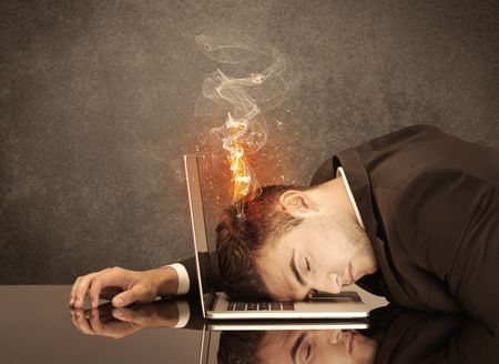 A frustrated businessman resting his head on a keyboard and shouting with his hair on smoke, catching fire