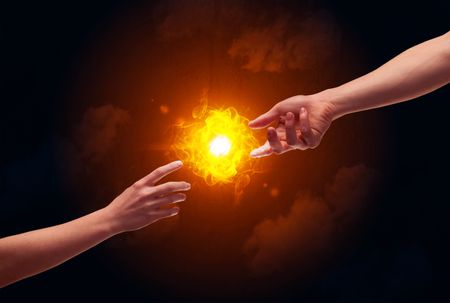 Two naked male hands about to touch, lighting a bright flame with smoke in red sky background concept