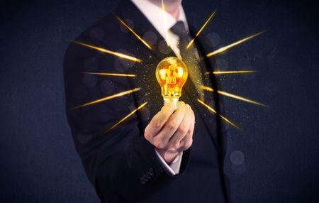 A male business person holding an electric light bulb in his hand with beam rays illustration concept.