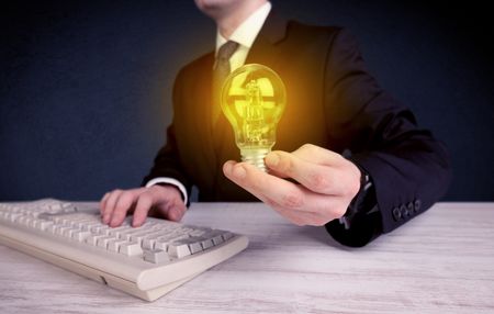 A business man in suit holding a glowing yellow light bulb in his hand while working in the office concept.