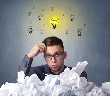 Young businessman sitting behind crumpled paper with lightbulbs above his head