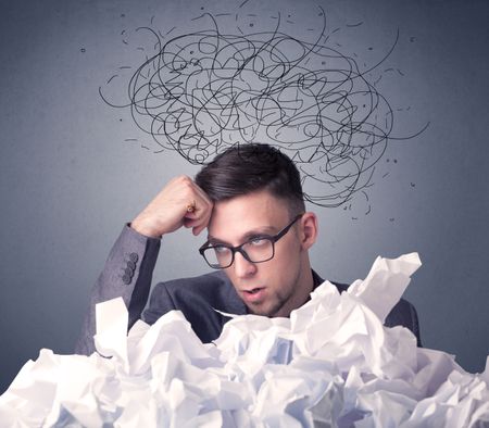 Young businessman sitting behind crumpled paper with scribbles over his head