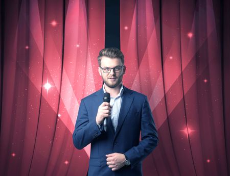 Businessman speaking into microphone with red curtain behind him 