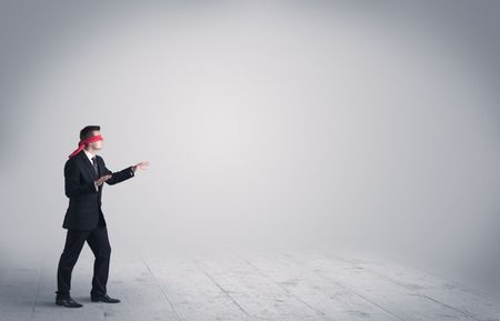 A young male business person in elegant dress standing with red blindfolds in a clear, empty space concept.