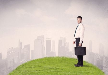 confident-male-well-looking-office-manager-648440815 A confident male well looking office manager standing in small green grass in front of city landscape with tall buildings concept.