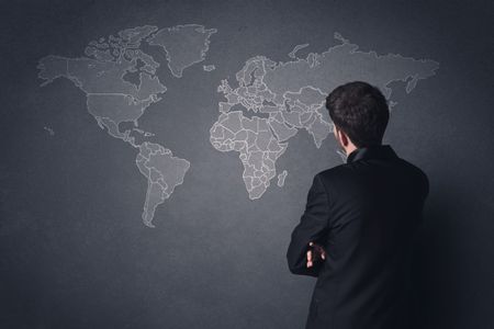 Young businessman in black suit standing in front of a black world map