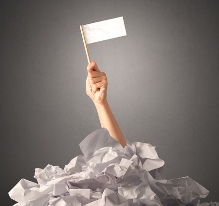 Female hand emerging from crumpled paper pile holding a white blank flag 