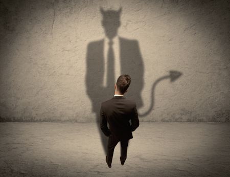 An experienced tricky businessman in suit looking at his devil desguise shadow reflected on the wall concept