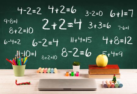 Going back to school concept with blackboard full of numbers and a busy student desk