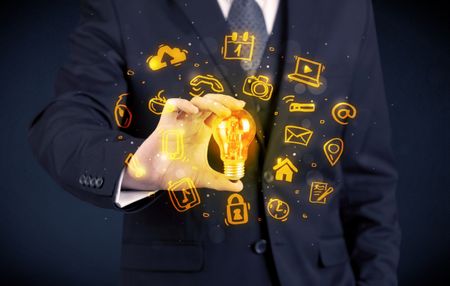 An office salesman promoting his bright ideas concept with illustration of online media and device logos around electric glass light bulb.