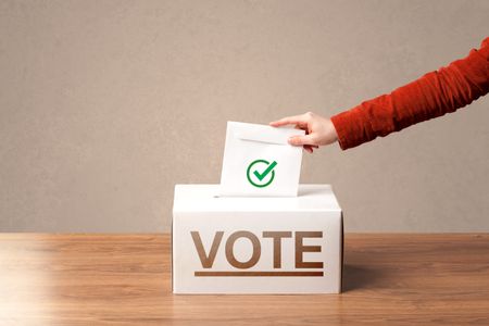 Close up of male hand putting vote into a ballot box, on grunge background