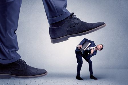 Young handsome businessman getting crushed by a big formal shoe
