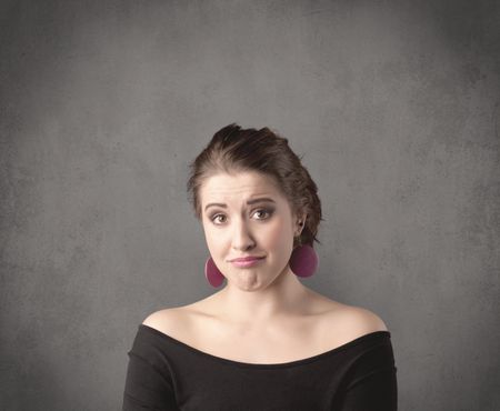 A pretty young teenage girl standing in front of a grey clear empty urban wall background concept while making funny faces.