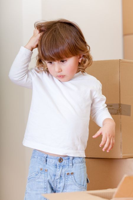 Confused little boy with cardboard boxes scratching his head