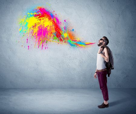 A funny hipster person in casual urban clothing shouting bright colorful paint on city wall concept