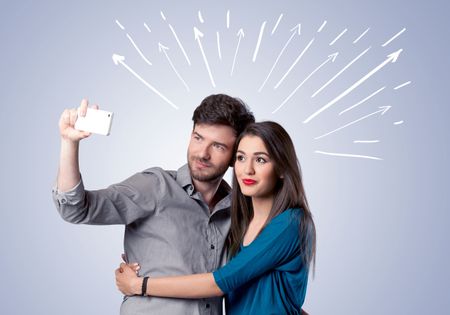 A cheerful young couple taking selfie photo with mobile phone and white lines and arrows pointing to the sky above them concept