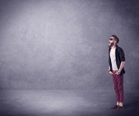 A hipster guy in stylish clothes shouting in front of an empty urban concrete wall background concept