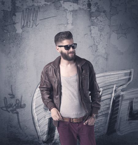 A handsome hipster guy with beard and sunglasses standing in front of an urban wall with graffiti concept
