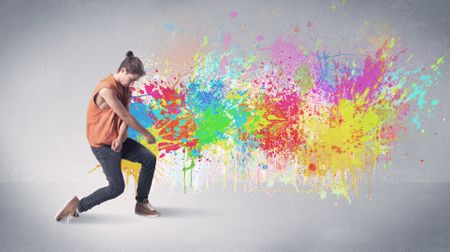 A funky contemporary hip hop dancer dancing in front of grey background with colorful bright paint splatter concept