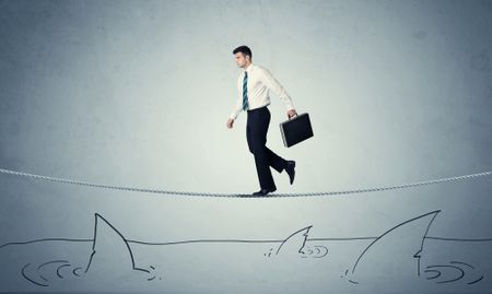 A brave businessman walking on tightrope expanded aboved rawn ocean with shark fin concept