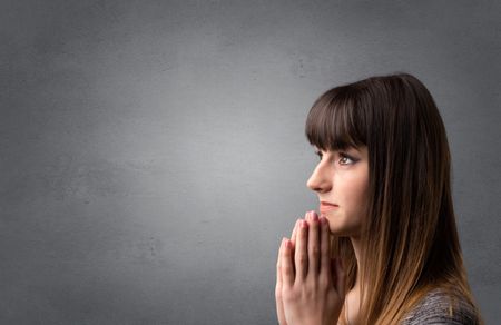 Young woman praying on a grey background