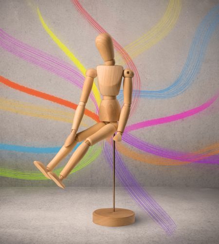 Wooden mannequin posed in front of a greyish background with colorful lines behind it