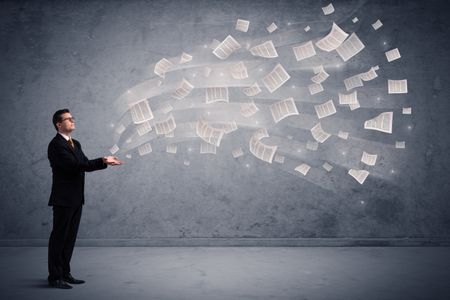 Caucasian businessman holding newspapers, which are floating away from his hands