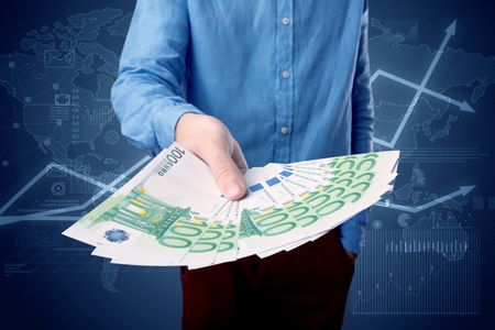 Young businessman holding large amount of bills with blue charts in the background