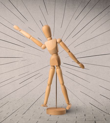 Wooden mannequin posed in front of a greyish background with black lines around him