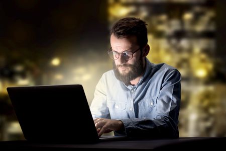 Young handsome businessman working late at night in the office with city lights in the background