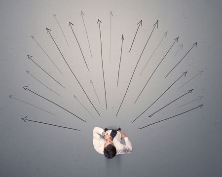 Young contemplating businessman stands in front of grey arrows 