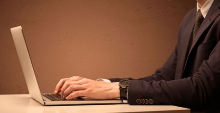 office-worker-elegant-suit-sitting-desk-654837076 An office worker in elegant suit sitting at desk, typing on portable laptop with empty brown wall background