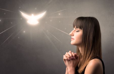 young-woman-praying-grey-background-sparkling-654855313 Young woman praying on a grey background with a sparkling bird above her