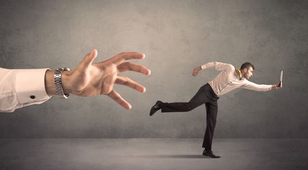 Young miniature businessman running from a big hand with grey background