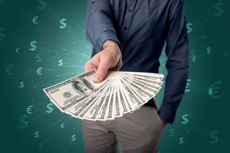 Young businessman holding large amount of bills with green background and currency symbols 