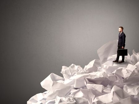 Thoughtful young businessman standing on a pile of crumpled paper with a deep grey background