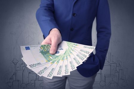 Young businessman holding large amount of bills with grungy drawings of a city and numbers behind him