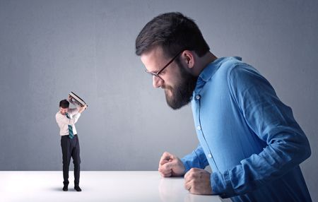 Young professional businessman being angry with an other miniature businessman in front of a blueish grey background