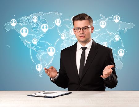 Young handsome businessman sitting at a desk with a blue world map behind him