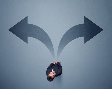 Young smart businessman standing in front of two arrows potinting to different ways contemplating a decision 