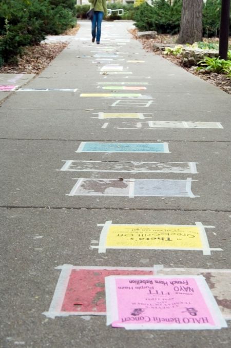 Student walks along campus sidewalk adorned with announcements