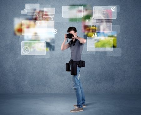 A young professional male photographer holding cameras and taking pictures in front of a blue wall with pictures, icons, text information concept