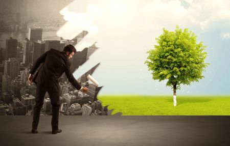 Businessman in elegant suit standing with his back, holding a roller and transforming the grey city landscape into green tree in bright nature environment concept