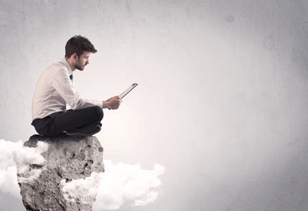 An elegant  smart businessman with laptop sitting in empty grey space on top of a cliff, between clouds concept