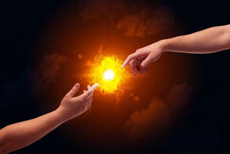Two naked male hands about to touch, lighting a bright flame with smoke in red sky background concept