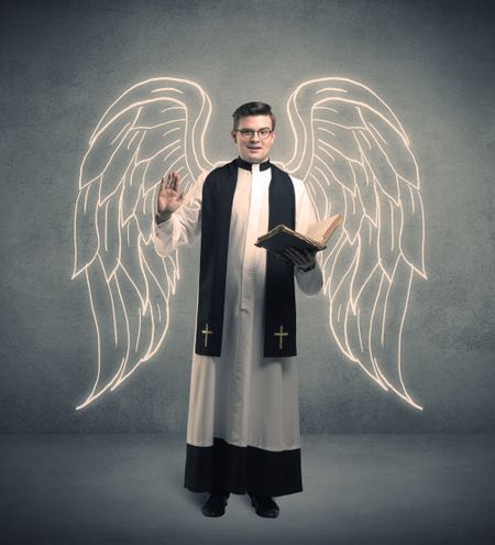 A young male priest with drawn large angel wings standing with the holy bible in his hands concept.