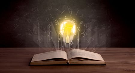 Shiny alphabet letters and yellow lightbulb hovering over open book 