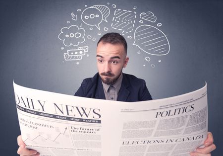 Puzzled young businessman reading daily newspaper with speech bubbles above his head