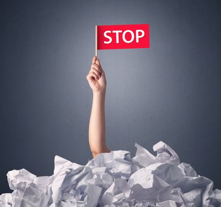 Female hand emerging from crumpled paper pile holding a red flag with stop written on it 