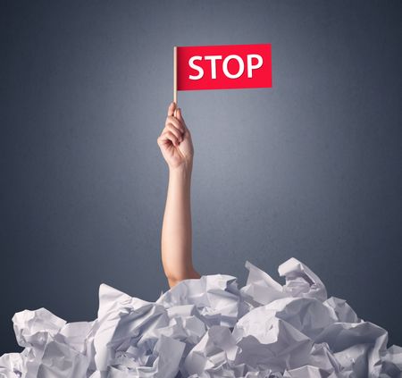 Female hand emerging from crumpled paper pile holding a red flag with stop written on it